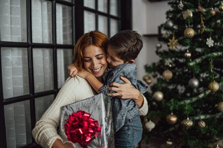 mother and son holding presents and hugging in front of Christmas tree